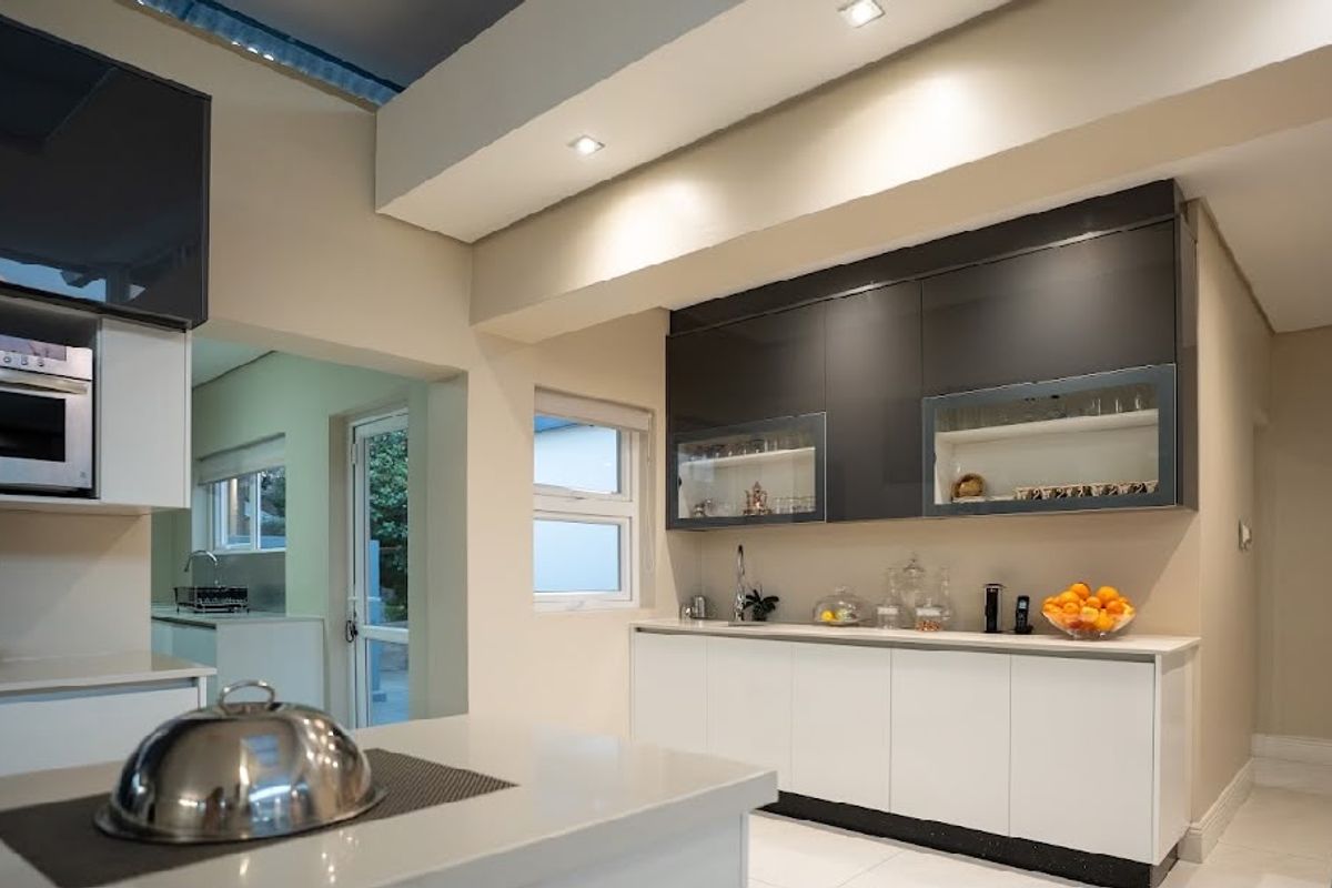 Modern kitchen featuring sleek two-tone cabinetry, stone countertops, integrated appliances, and recessed lighting with natural light from a skylight.