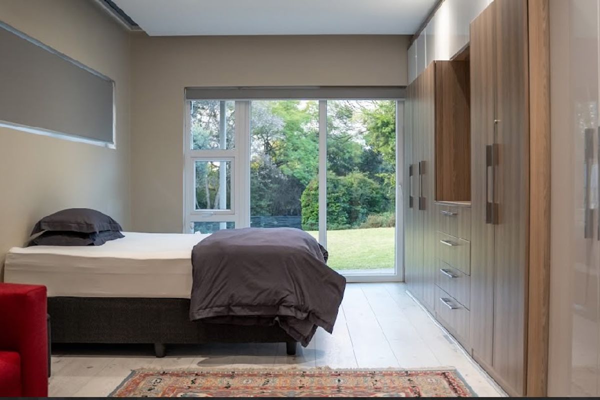 A modern bedroom featuring extensive built-in cabinetry, light timber flooring, and a large sliding glass door providing direct access to the garden.