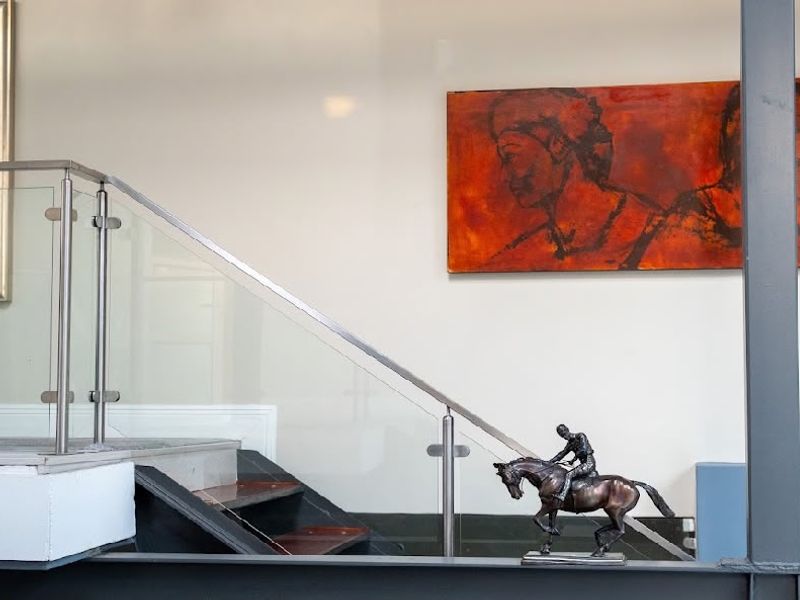 A modern hallway featuring a timber staircase with a sleek glass balustrade and stainless steel handrail, supported by a prominent steel structural beam.