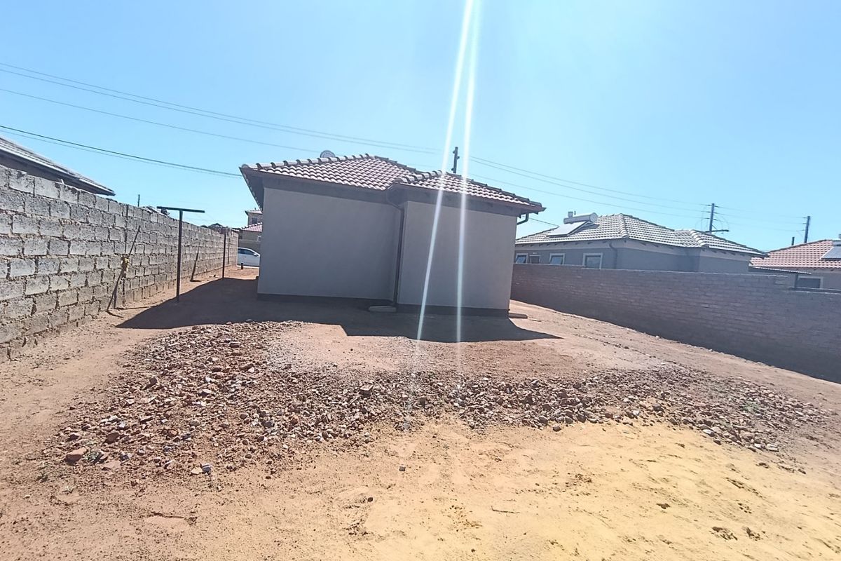 Rear view of the property featuring a tiled roof, solar water heater, and a large, undeveloped backyard enclosed by perimeter boundary walls.