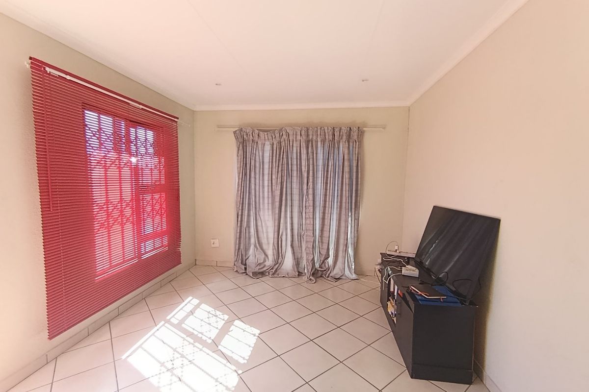 A living room featuring neutral tiled flooring, window blinds, and security gates, providing a functional and well-lit space.