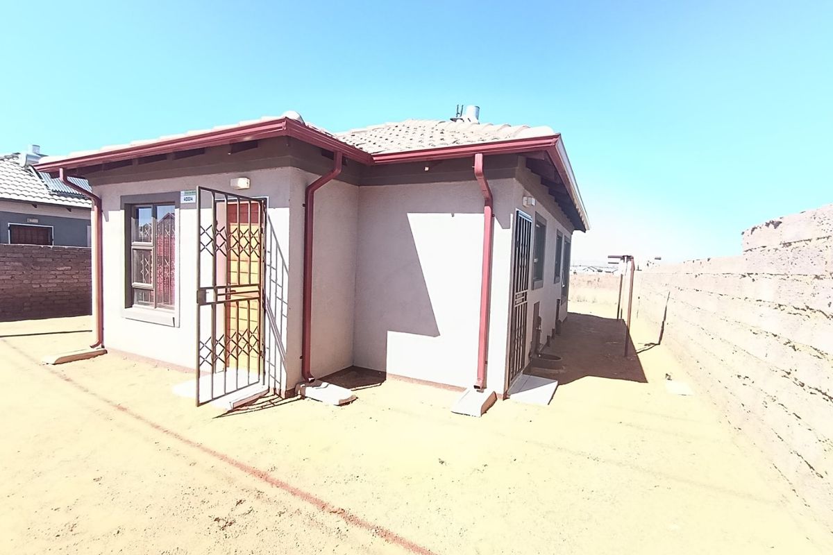 Rear view of a detached house featuring a tiled roof, security gates, and a surrounding boundary wall on an unpaved plot.