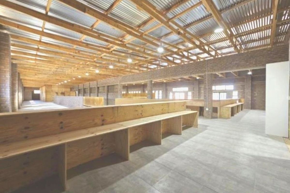Spacious utility area featuring exposed timber roof trusses, corrugated metal ceiling, face brick walls, and extensive built-in timber counters on tiled flooring.