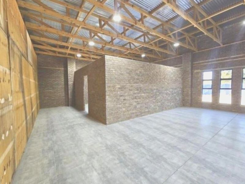 A spacious, open-plan utility area featuring exposed timber roof trusses, face brick walls, and modern tiled flooring, offering versatile potential for various uses.