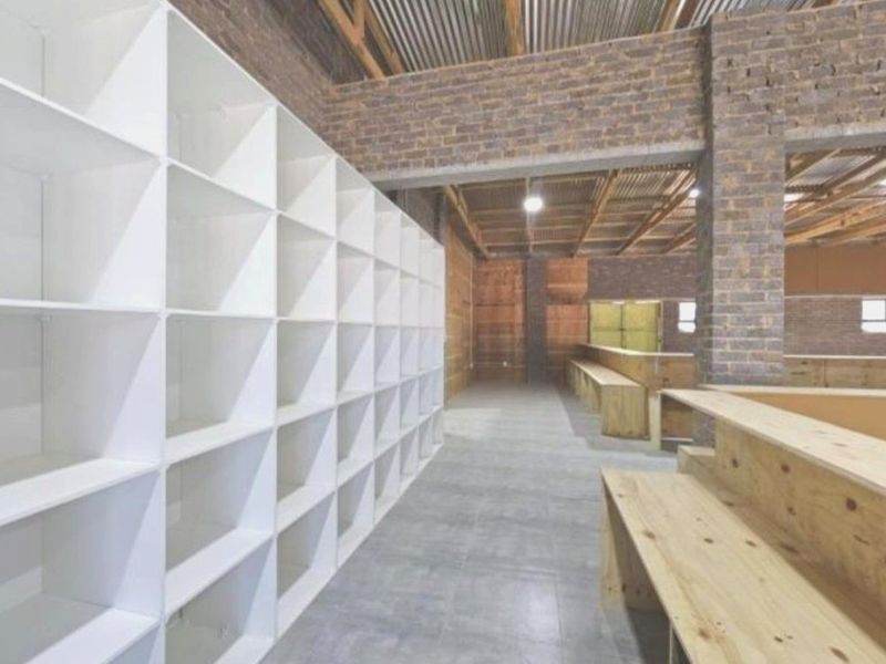 Spacious utility area featuring exposed brickwork, high timber-trussed ceilings, tiled flooring, and extensive built-in white shelving units.