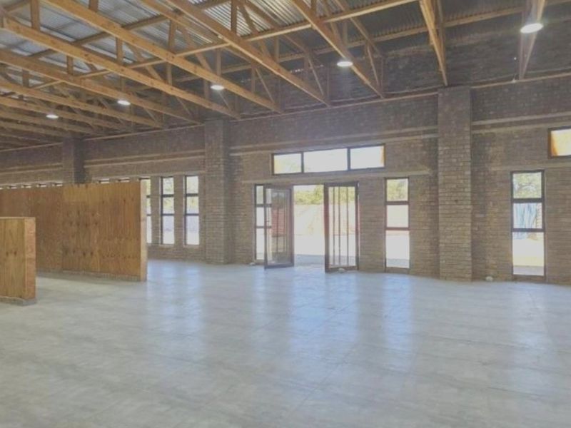 Spacious industrial-style utility area featuring exposed timber roof trusses, face brick walls, polished concrete floors, and large aluminium-framed glass doors.