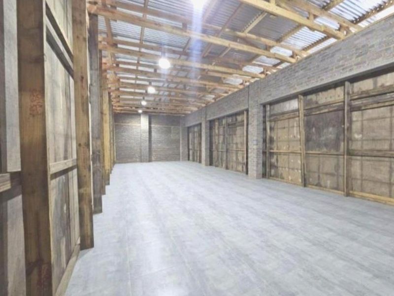 A spacious, open-plan utility or storage area featuring exposed timber roof trusses, brick walls, and durable concrete flooring, suitable for various agricultural or workshop uses.