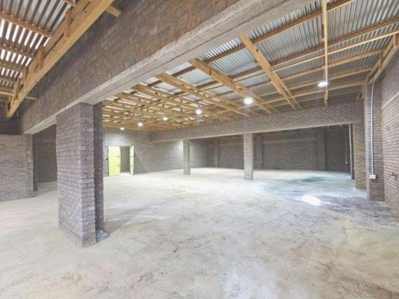 A large, open-plan utility or storage space featuring exposed brick walls, timber roof trusses, and a concrete floor, suitable for various commercial or agricultural uses.