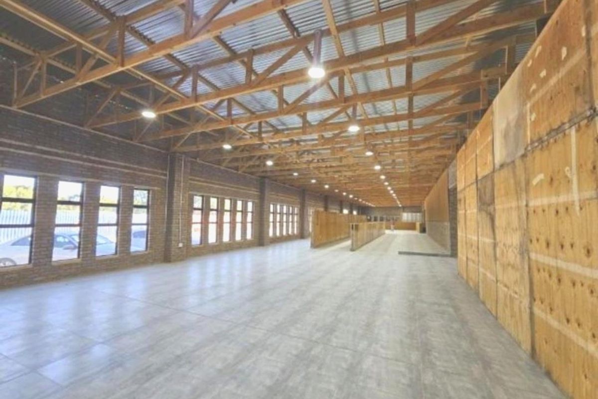 A large, open-plan utility or commercial space featuring exposed timber roof trusses, tiled flooring, and extensive natural light through multiple windows.