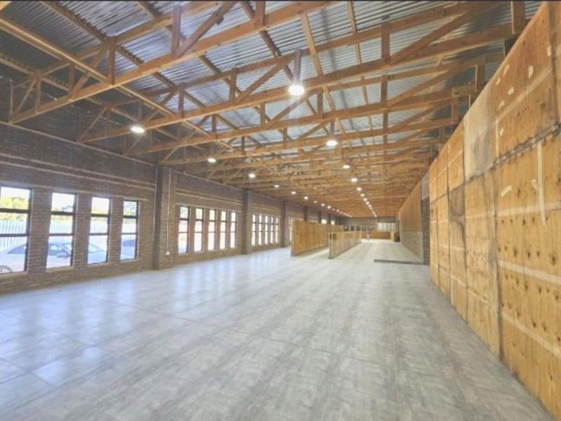 A large, open-plan utility or commercial space featuring exposed timber roof trusses, tiled flooring, and extensive natural light through multiple windows.