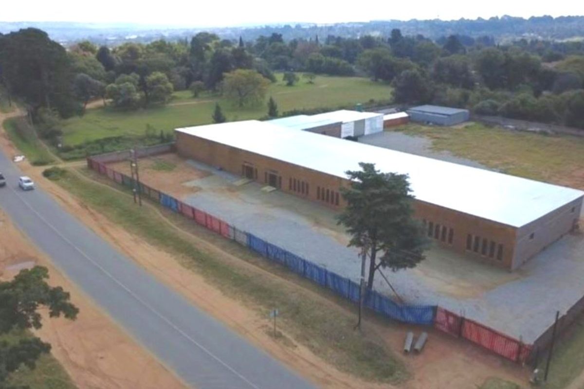 Aerial view of a large industrial or farm-style building with a metal roof, situated on a spacious plot adjacent to a public road.