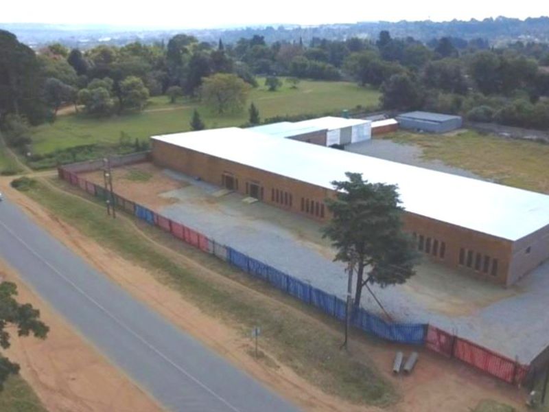 Aerial view of a large industrial or farm-style building with a metal roof, situated on a spacious plot adjacent to a public road.