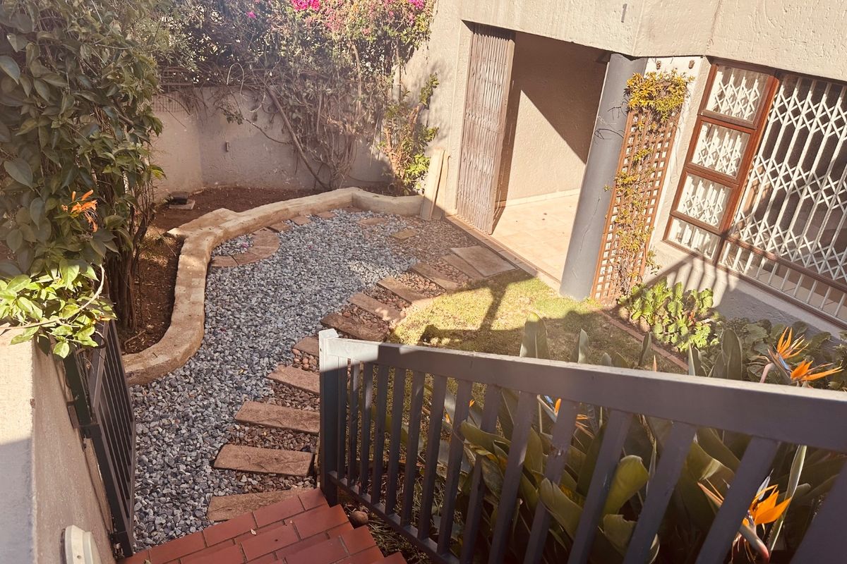 A rear courtyard area featuring a gravel garden, stone retaining wall, and brick staircase leading to a covered patio with security gates.