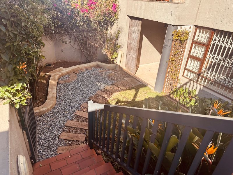 A rear courtyard area featuring a gravel garden, stone retaining wall, and brick staircase leading to a covered patio with security gates.