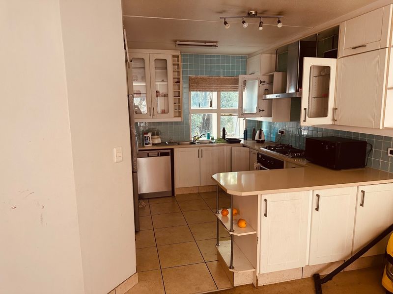 A functional kitchen featuring built-in cabinetry, a tiled backsplash, gas hob, and a breakfast counter, offering a practical layout with potential for modern updates.