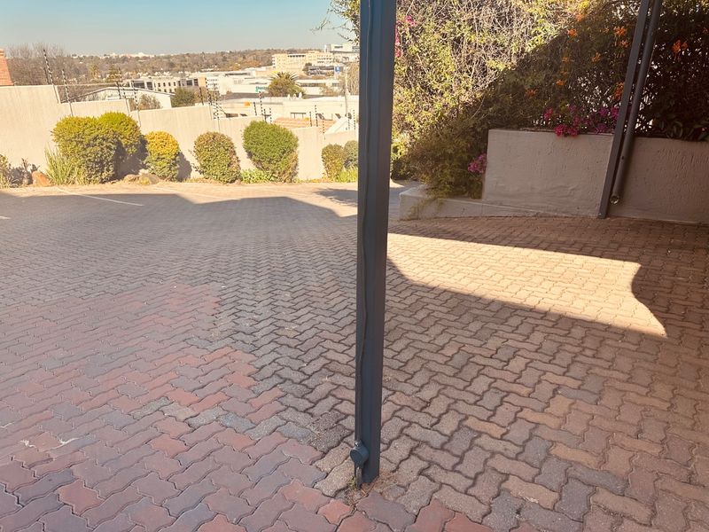 A paved driveway area featuring a carport support pillar, retaining wall, and perimeter electric fencing with views of the surrounding neighborhood.