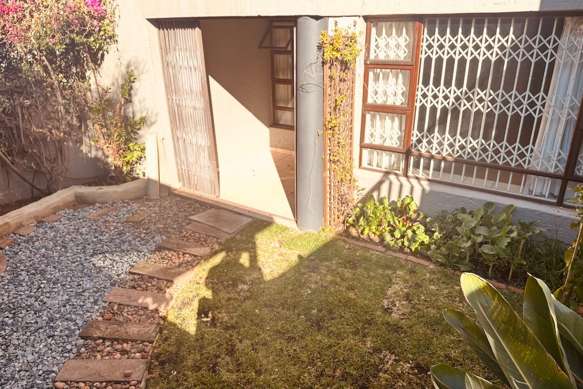 Rear exterior view of the townhouse featuring a small garden, paved walkway, security gates, and window security bars.