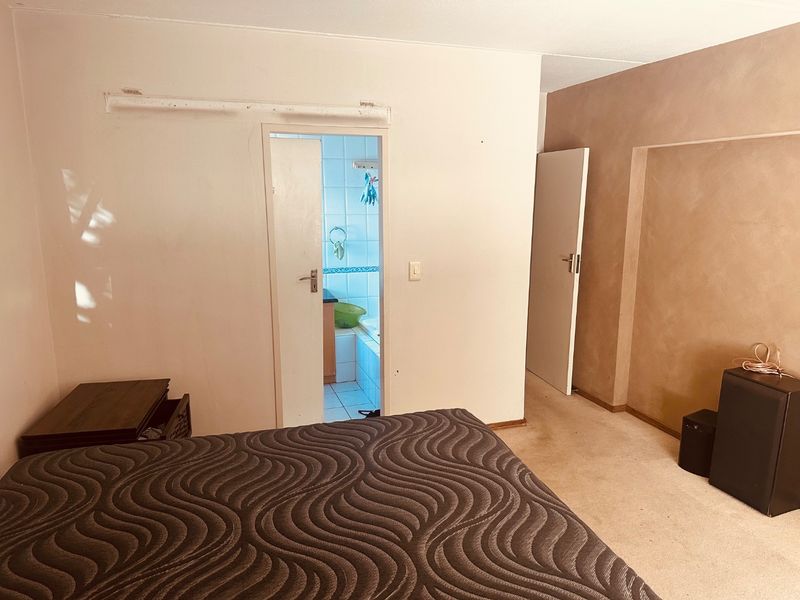 A bedroom featuring carpeted flooring and direct access to an en-suite bathroom, requiring cosmetic updates to wall finishes and flooring.