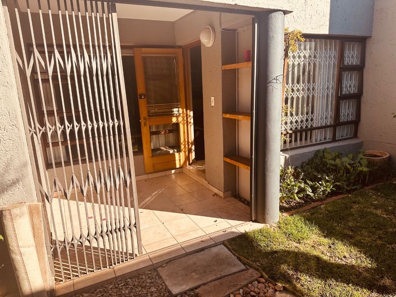 A covered patio area featuring tiled flooring, built-in shelving, and security gates, providing a functional transition space between the interior and the garden.