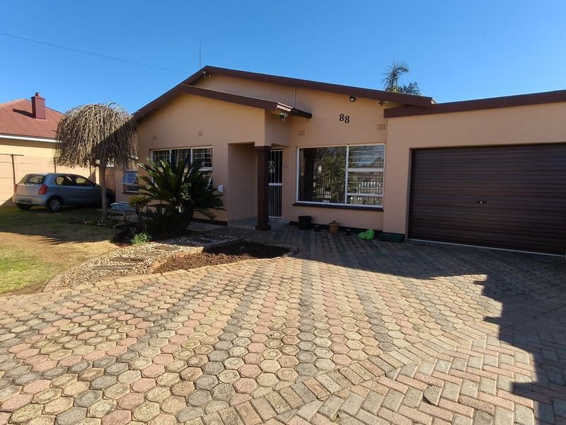 Front view of a single-story house featuring a paved driveway, integrated single garage, and established garden area.