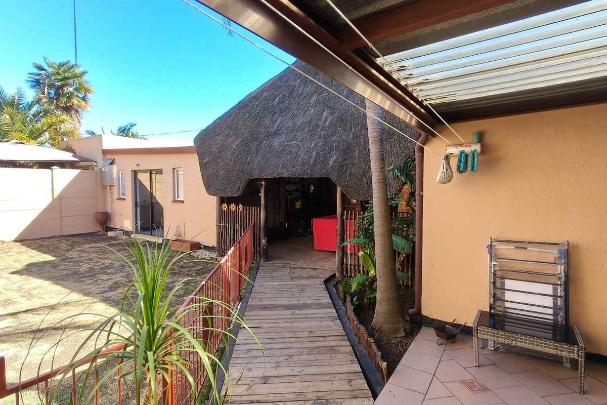 Rear exterior view featuring a thatched roof structure, timber walkway, tiled patio area, and a small garden space.