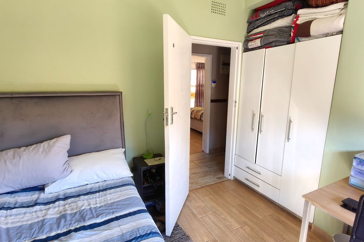 A bedroom featuring light green walls, tiled flooring, and a white built-in wardrobe with overhead storage space.