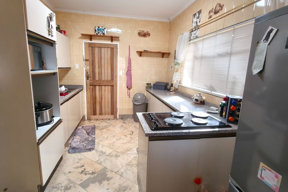 A functional kitchen featuring built-in cabinetry, granite countertops, an electric hob, and tiled finishes throughout.