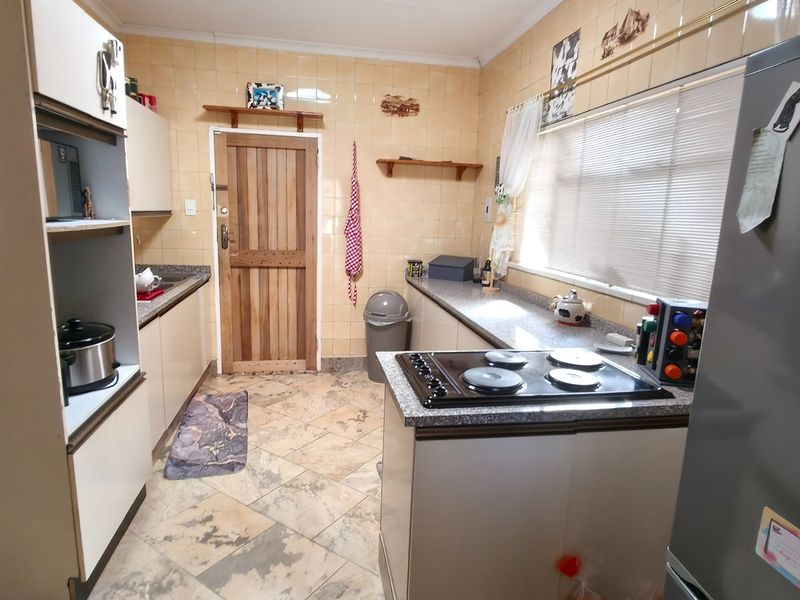 A functional kitchen featuring built-in cabinetry, granite countertops, an electric hob, and tiled finishes throughout.
