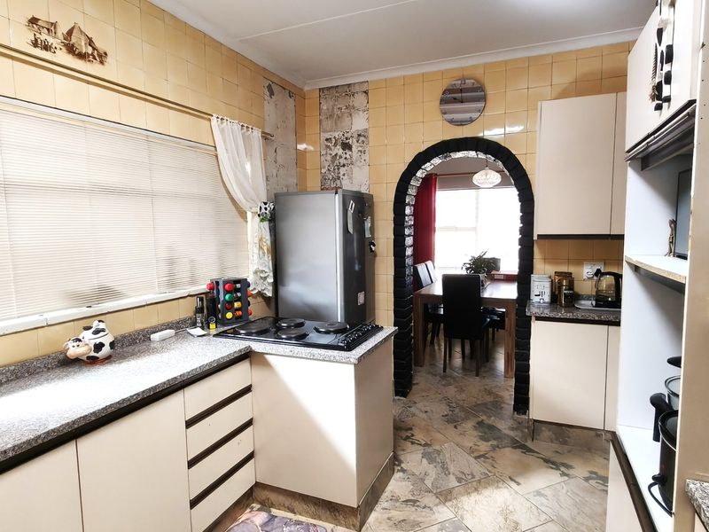A dated kitchen featuring tiled walls, laminate countertops, and an electric hob, with an arched opening leading to the dining area.