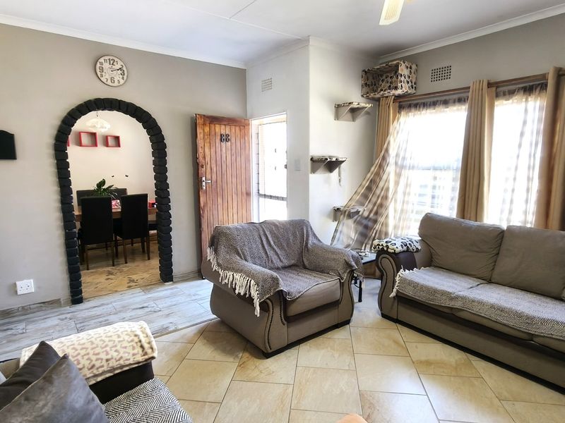A living room featuring tiled flooring, a distinctive arched doorway leading to the dining area, and a ceiling fan.