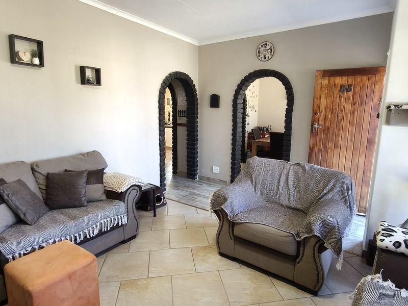 A living room featuring tiled flooring and distinctive arched doorways with exposed brick detailing, leading to adjacent living spaces.