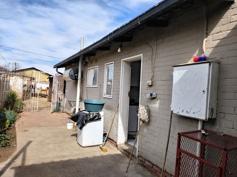 Rear exterior view of the property showing brick wall, mounted electric geyser, electrical distribution box, and concrete paved area.