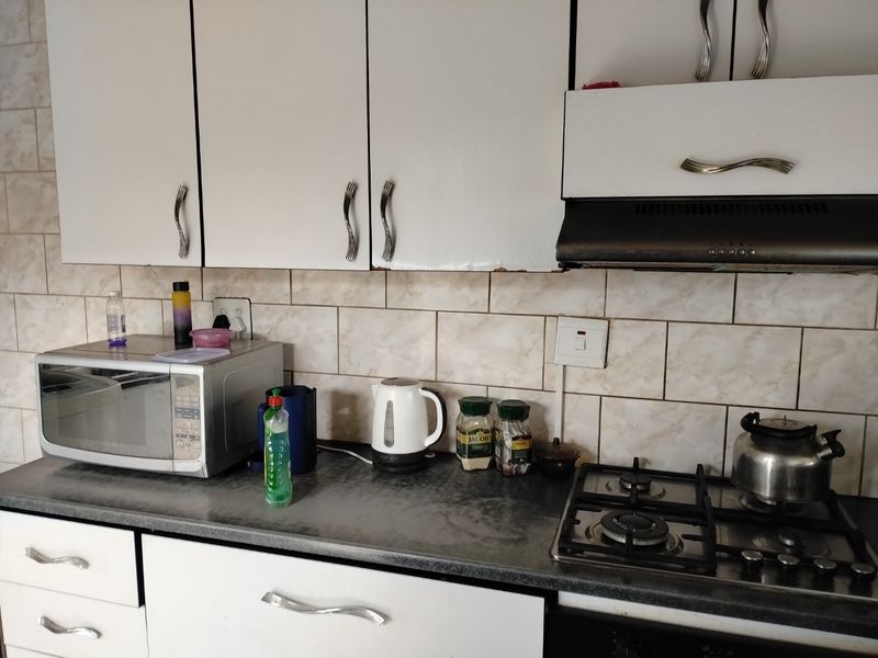 A functional kitchen area featuring white cabinetry, a gas hob with extractor fan, and tiled backsplash with a dark laminate countertop.