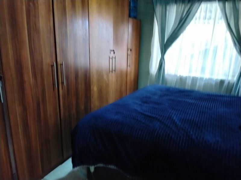 A bedroom featuring a large built-in wooden wardrobe and a window with curtains.