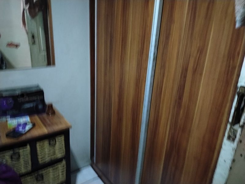 A bedroom featuring a wood-finish built-in wardrobe with sliding doors, showing signs of wear and dated finishes.