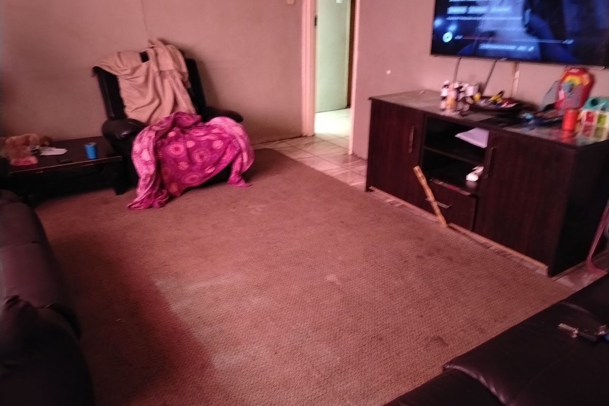 A living room area featuring tiled flooring and access to an adjacent room, currently showing signs of wear on the carpet and wall surfaces.