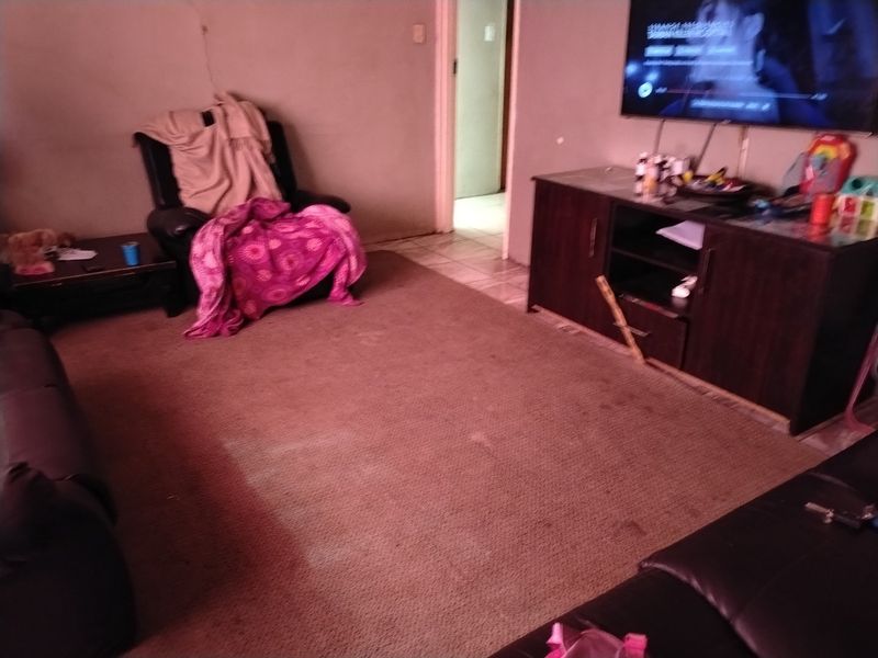 A living room area featuring tiled flooring and access to an adjacent room, currently showing signs of wear on the carpet and wall surfaces.