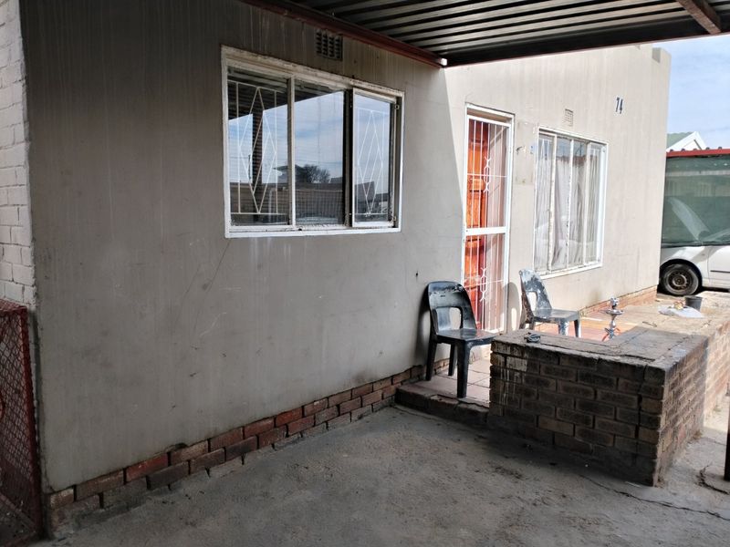 A covered outdoor patio area featuring a concrete floor, brick base wall, and security gate access to the main dwelling.
