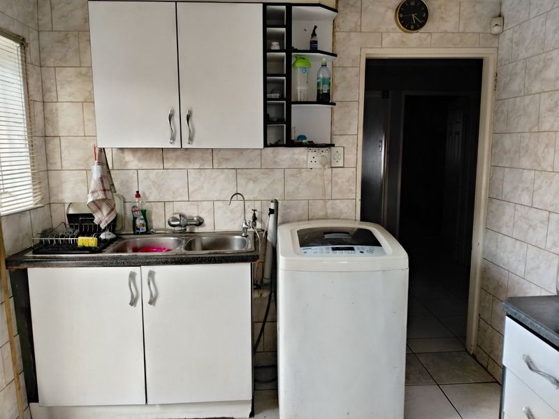 A functional scullery area featuring a double bowl sink, wall-mounted cabinetry, and tiled finishes, providing practical utility space for food preparation and laundry tasks.