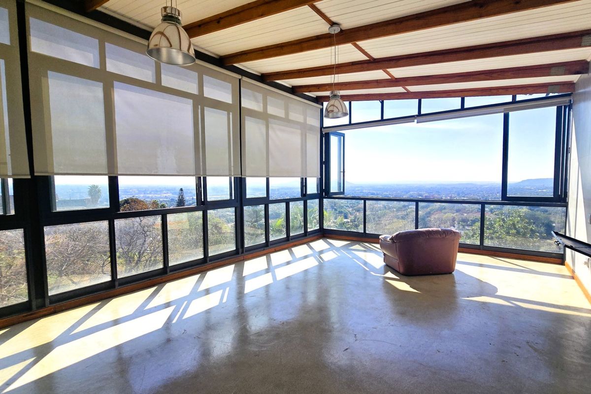 Spacious sunroom featuring polished concrete floors, exposed timber beams, a built-in fireplace, and expansive windows offering panoramic views.