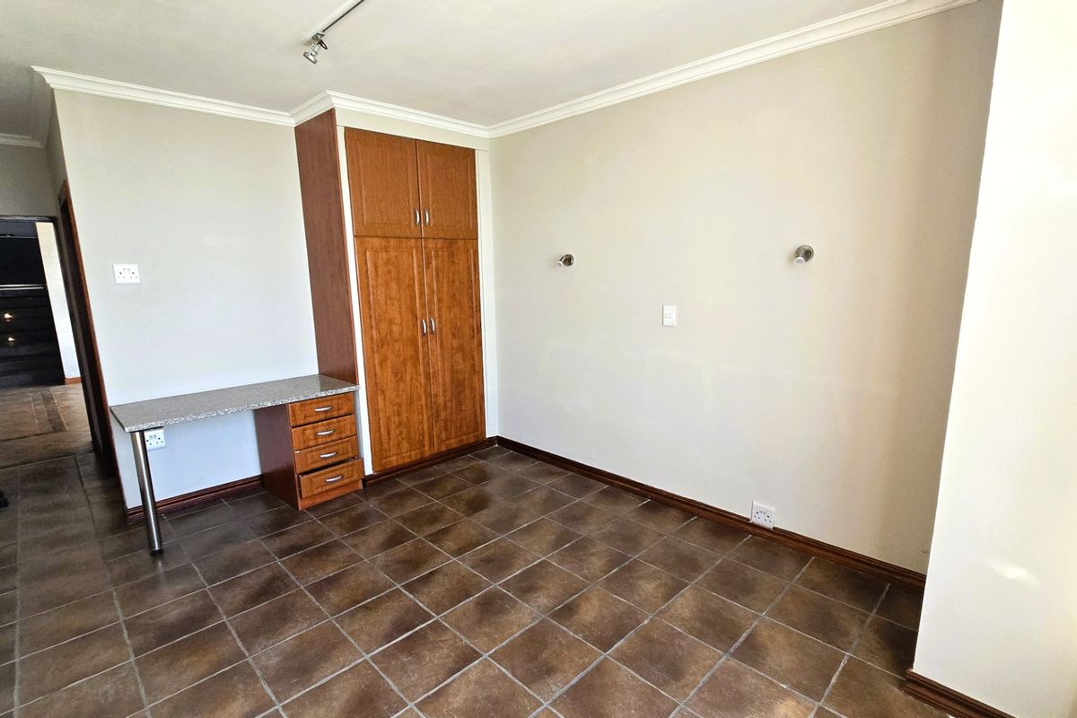 A clean, empty bedroom featuring tiled flooring, a built-in wooden wardrobe, and a matching built-in desk unit.