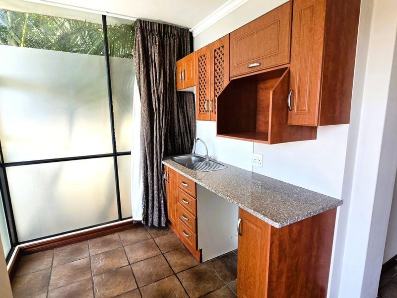 A functional scullery area featuring built-in wooden cabinetry, a granite countertop, and a stainless steel sink, set against a large window.