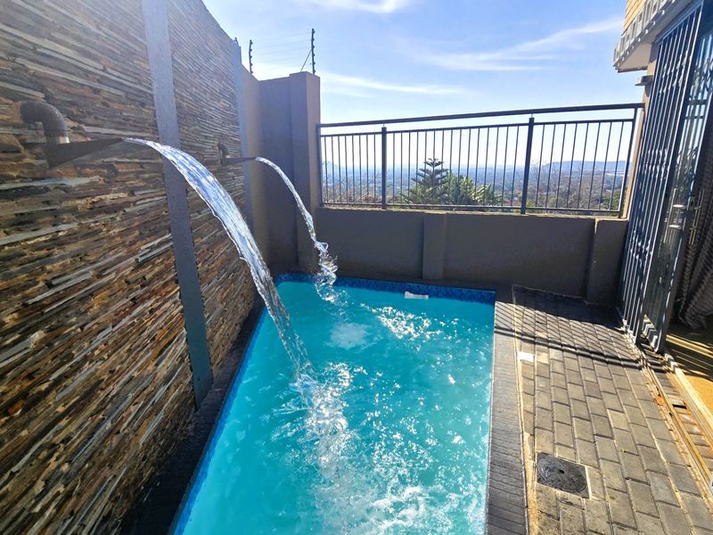 A compact swimming pool area featuring a stone-clad water feature, paved surround, and metal security fencing with elevated views.