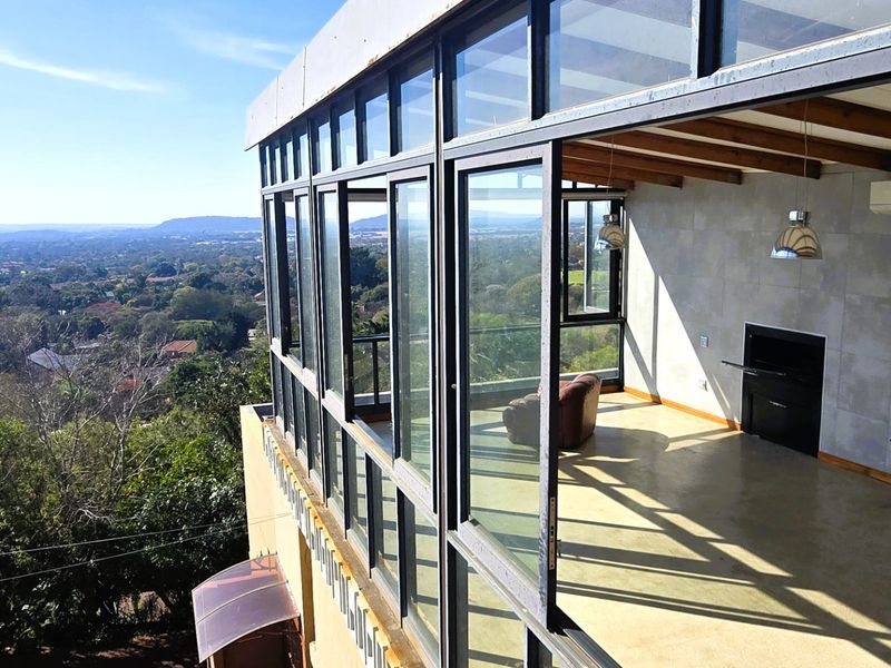Spacious elevated balcony featuring polished concrete floors, exposed timber beams, a built-in fireplace, and expansive glass walls offering panoramic views.
