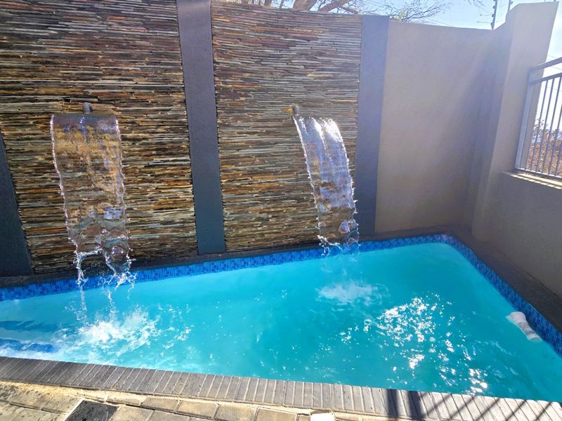 A compact swimming pool featuring a decorative stone-clad wall with integrated water features and modern metal safety railings.
