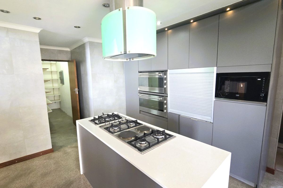 Modern kitchen featuring a central island with a combination gas and electric hob, built-in double ovens, integrated microwave, and an adjacent walk-in pantry.