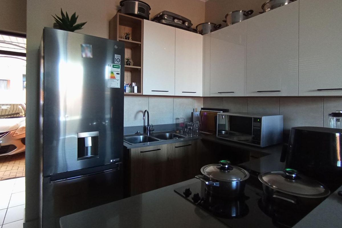 A modern kitchen featuring white gloss cabinetry, stone countertops, a double sink, and a built-in electric hob with direct access to the exterior.