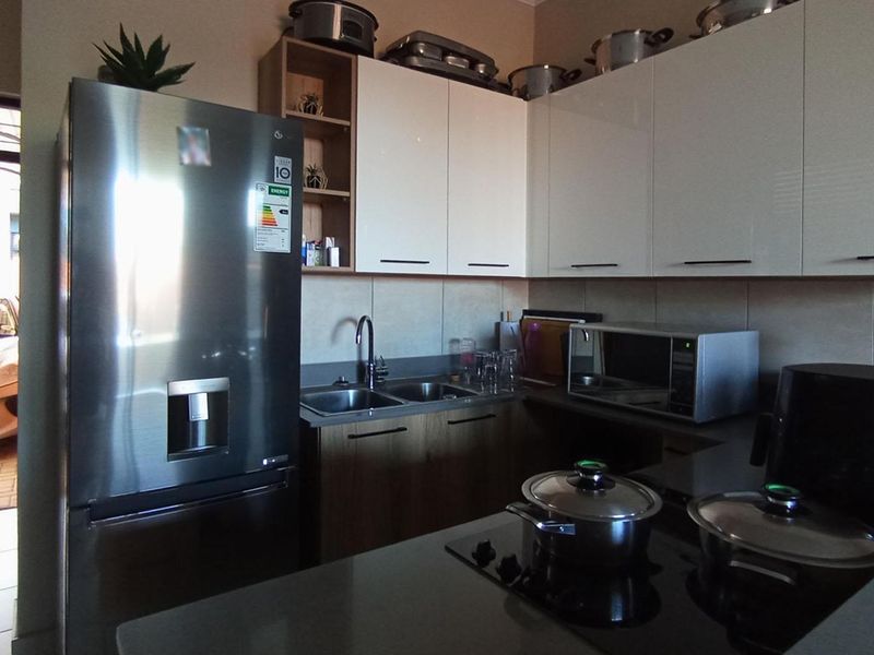 A modern kitchen featuring white gloss cabinetry, stone countertops, a double sink, and a built-in electric hob with direct access to the exterior.