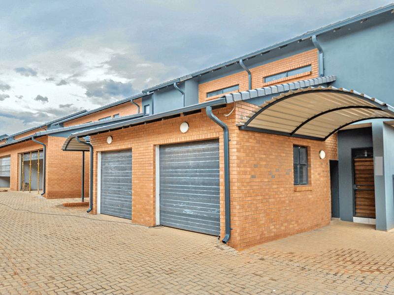 Front elevation of a modern townhouse complex featuring face brick construction, roller shutter garage doors, and covered entrance walkways with paved driveway access.