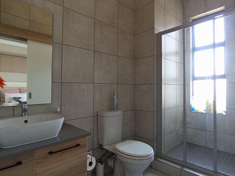 A modern bathroom featuring a vessel sink on a wooden vanity, a toilet, and a glass-enclosed shower with neutral wall tiling.